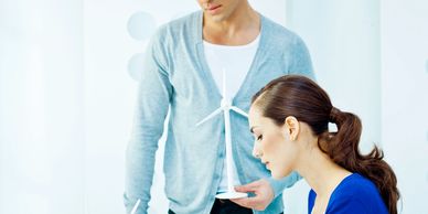 A man in a gray cardigan standing beside a woman in blue focused on her work.