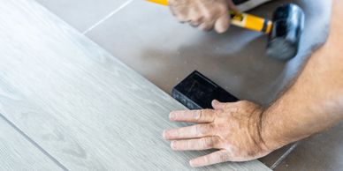 Hands installing wooden flooring with a rubber mallet.