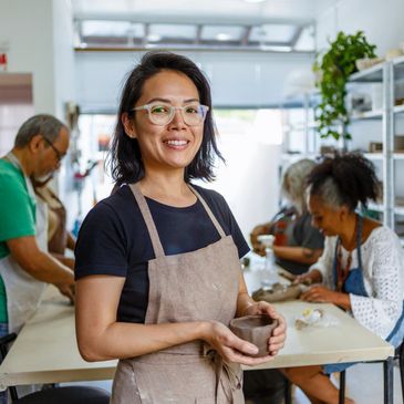 Smiling woman holding a clay pot in a pottery class.