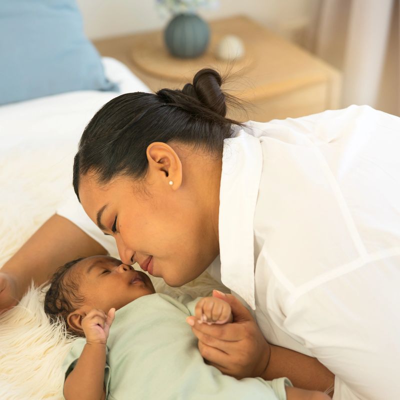 Portrait happy smiling of a beautiful Asian mother kissing nose-to-nose newborn baby son 1-month-old,  and looking at him with love. Adorable little infant sleep well in warm embrace of motherhood.