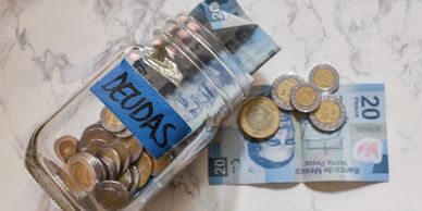 A jar labeled 'DEUDAS' with Mexican coins and 20 peso bills spilling out.