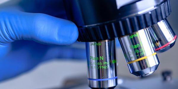Close-up of gloved hand adjusting microscope lenses in a lab.