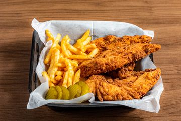 Basket with crispy fried chicken tenders, crinkle-cut fries, and pickle slices.