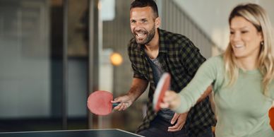 Two people enthusiastically playing ping pong indoors.