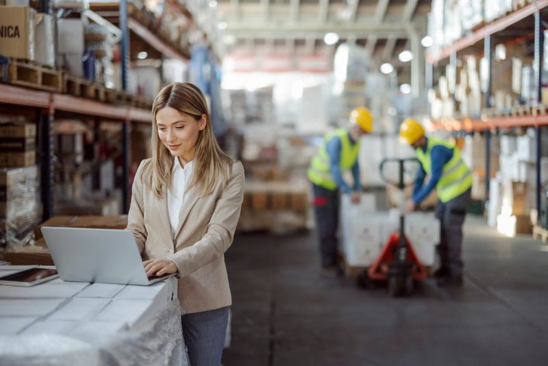 Female inventory manager working with computer laptop in storage warehouse. People, warehouse and industry concept