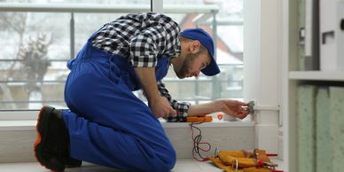 A handyman kneeling, fixing some wood trim.