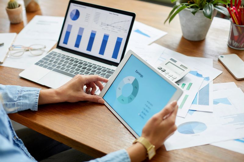 Hands of businesswoman holding digital tablet with diagram. Young entrepreneur is working at home. She is analyzing financial charts.