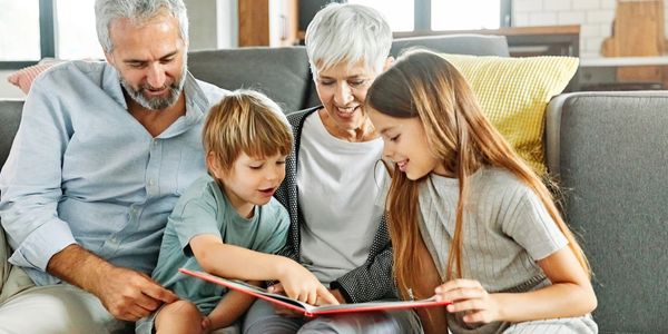Grandparents reading a book with their grandchildren on the couch.