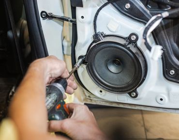 Person installing or repairing a car door speaker with a screwdriver.