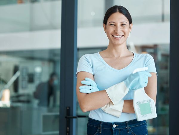 Smiling woman wearing cleaning gloves and holding a spray bottle.