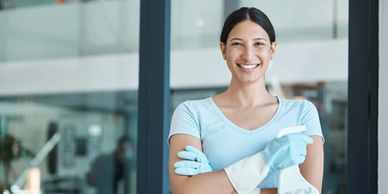 Smiling woman in blue gloves holding cleaning spray and cloth.