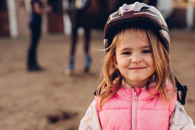Smiling girl in a pink vest and helmet standing outdoors.