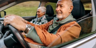 Smiling elderly man driving with a woman passenger.