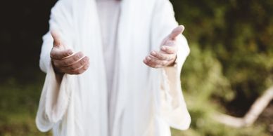 Person in white robe with outstretched hands, inviting or offering.