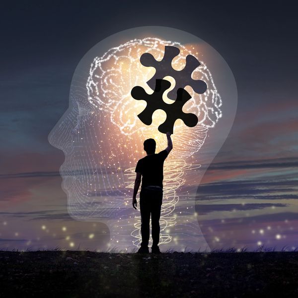 Silhouette placing puzzle pieces into a glowing brain inside a head outline.