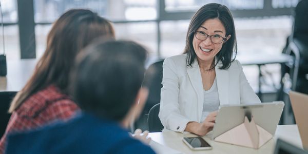 Woman in white blazer leading a meeting with colleagues.