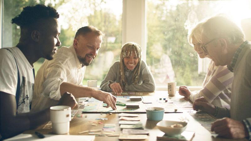 Diverse family with african-american children and elderly parents having fun together. Playing a board game with cards and dice. Family fun afternoon.