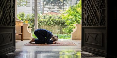 A person praying on a rug in a serene outdoor space framed by open doors.