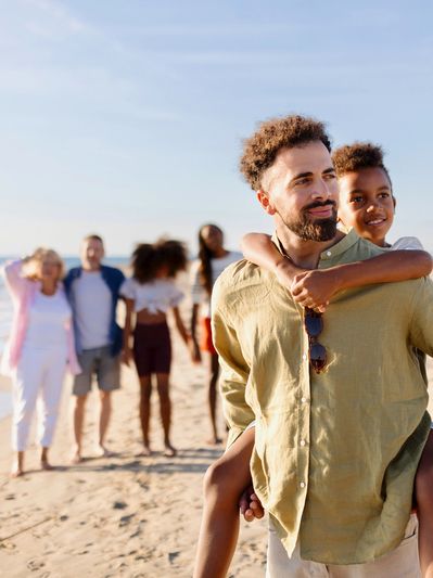 An adult man in the forefront with younger and older family members in the background on a beach.