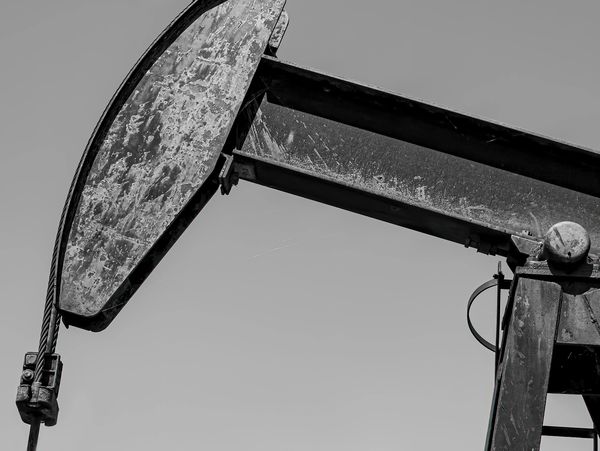 Close-up of a weathered oil pumpjack against a clear sky.