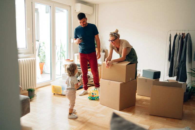 Happy family with one child drinking coffee and talking while unpacking boxes in new home on moving day.