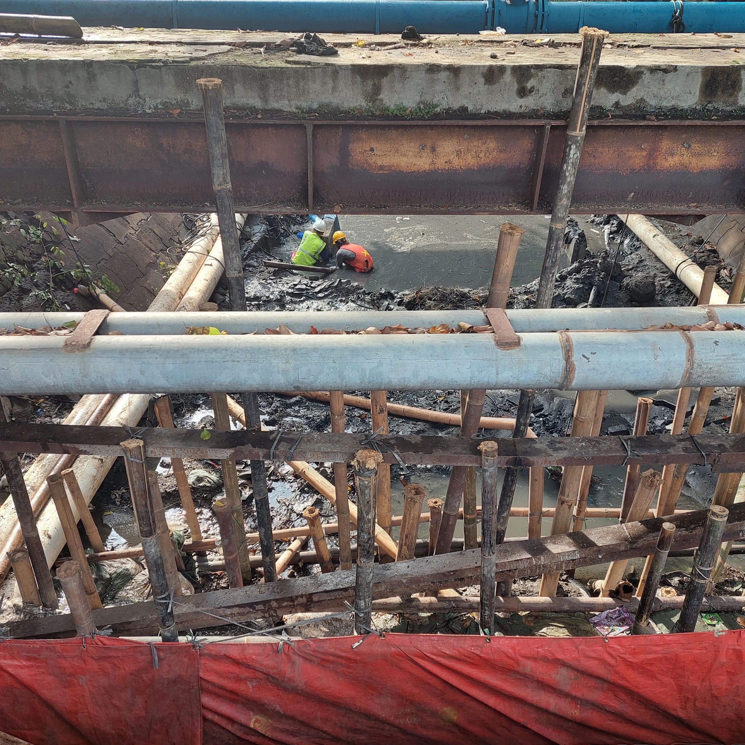 Workers in safety gear working in a muddy construction site beneath a bridge.