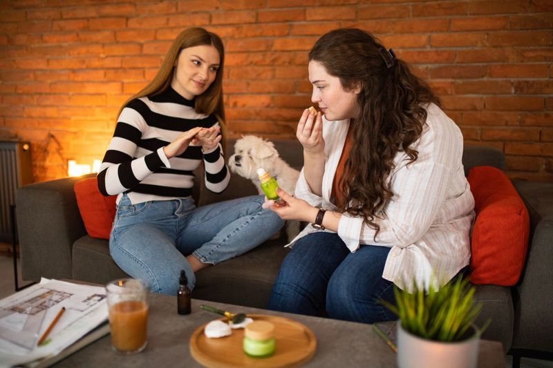 Two female friends using hand cream in living room at home