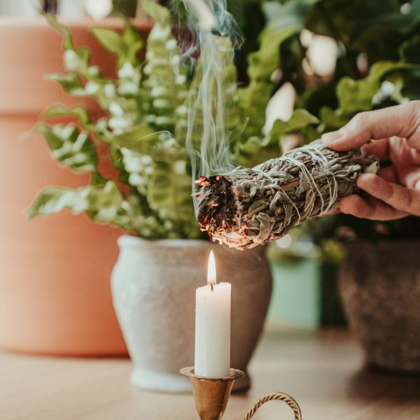 Burning sage stick near a lit candle indoors.
