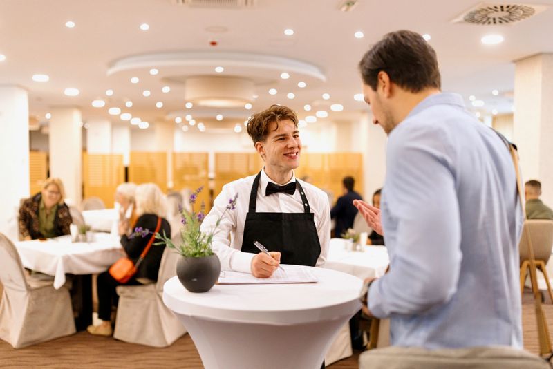Waiter looks at the guest checklist and greets the hotel guests during breakfast