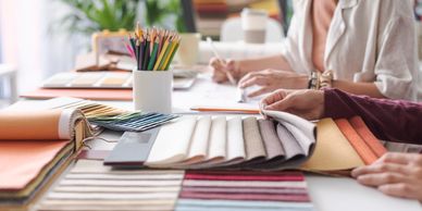 Two designers reviewing fabric swatches and color pencils at a creative workspace.