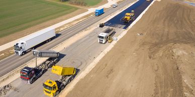 Construction trucks working on a highway expansion project beside active traffic.