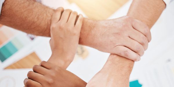 An image of the arms and hands of four people linking together in a closed circle.