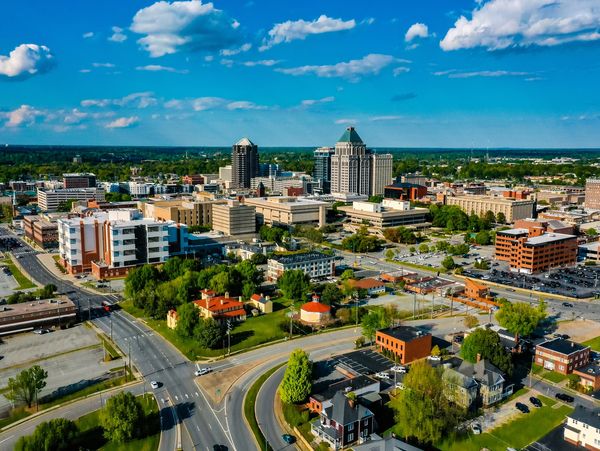 Aerial view of a cityscape with buildings, roads, and greenery under a blue sky.