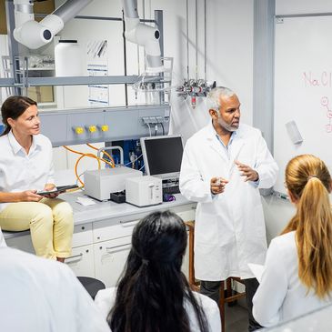 Scientists discussing chemical formulas around a whiteboard.