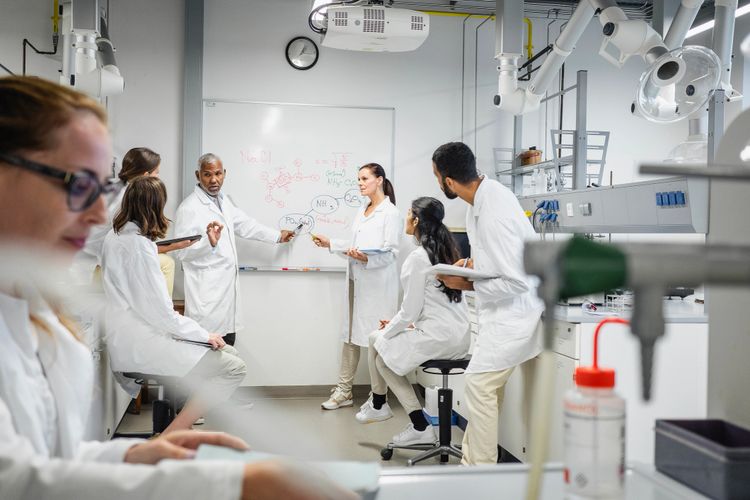Scientists in lab coats discuss chemical formulas in a laboratory.