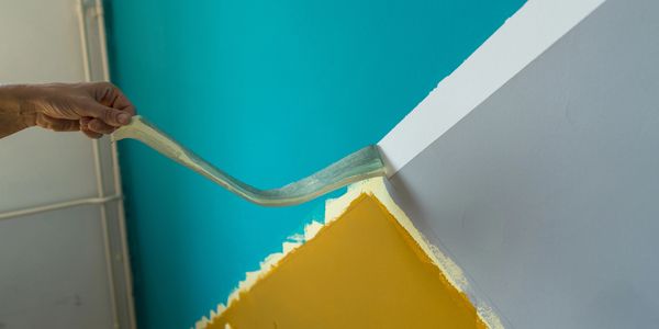 Hand peeling off tape from a freshly painted wall with turquoise, white, and yellow sections.