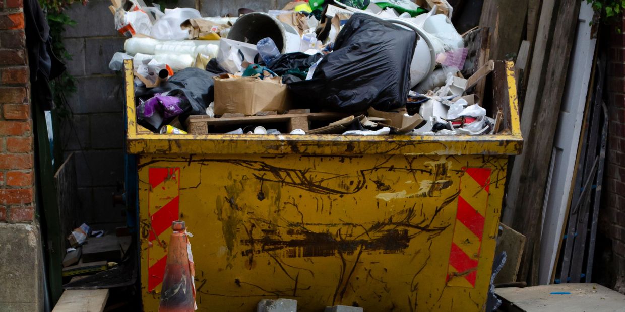 A yellow dumpster overflowing with mixed trash and debris.