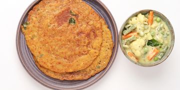 Two crispy Indian flatbreads with a bowl of mixed vegetable curry.