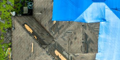 A roof with a damaged section covered by a blue tarp.