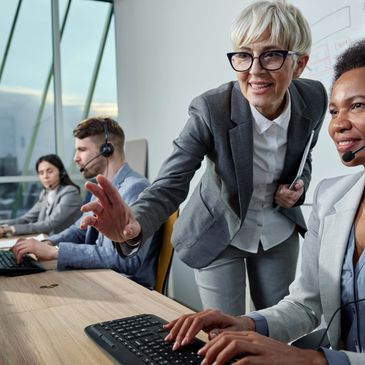 Senior woman mentoring a female colleague in a busy call center environment.