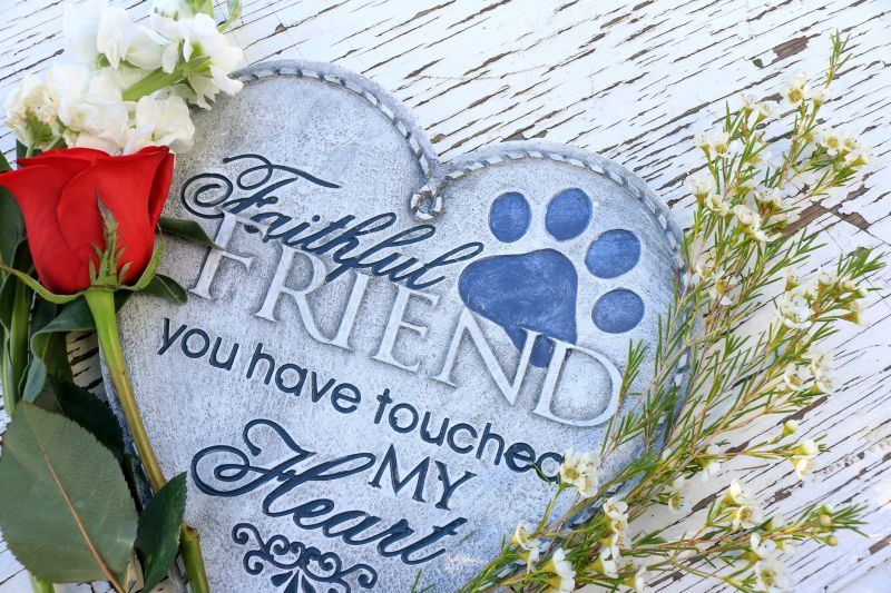 Flowers and a red rose surrounding a heart shaped plaque. Loss of a beloved pet.