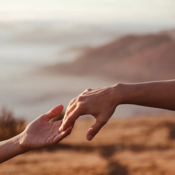 Two hands gently reaching out in a warm, natural setting.