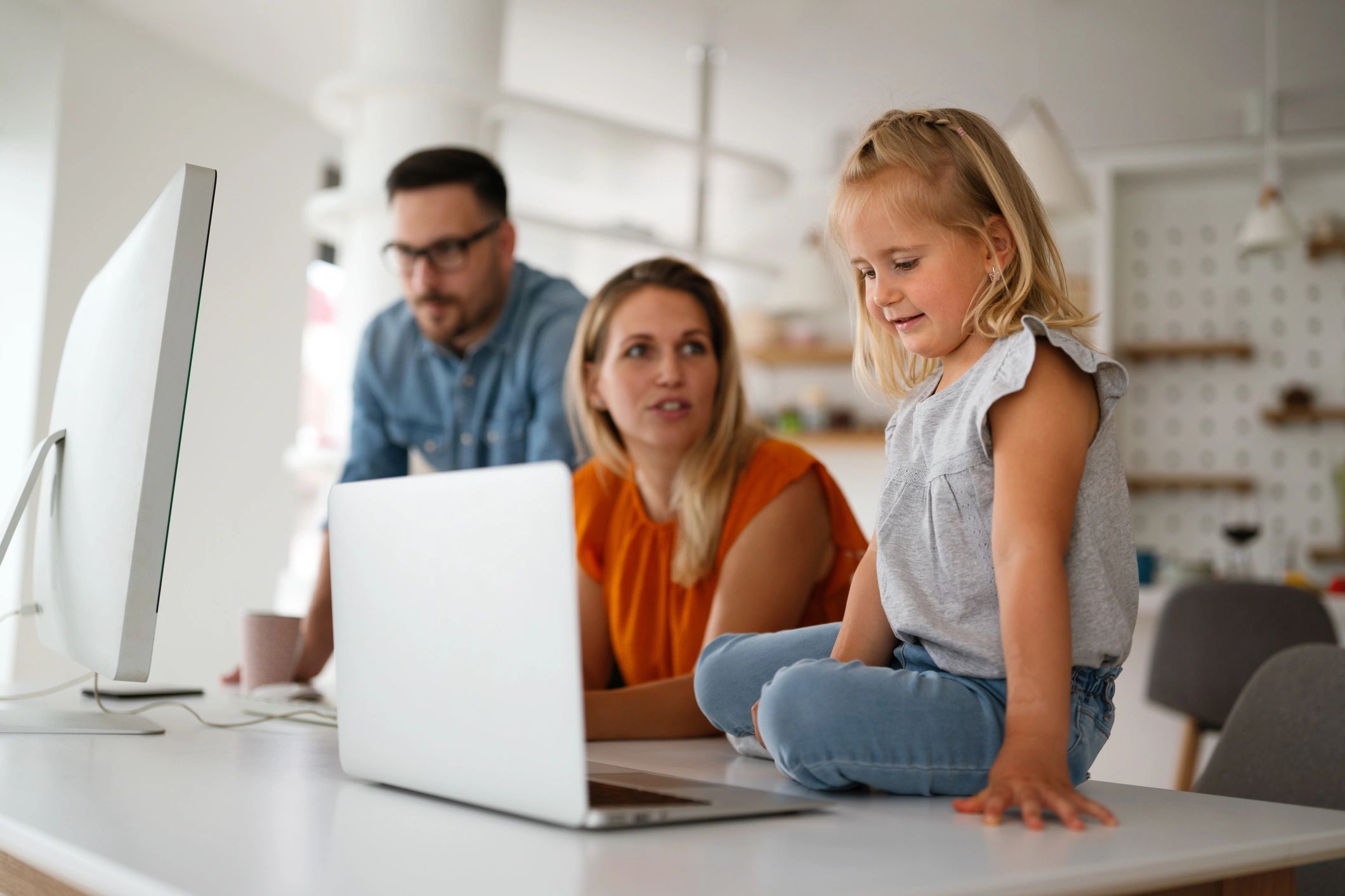 Smiling little girl with parents working on computers at home.