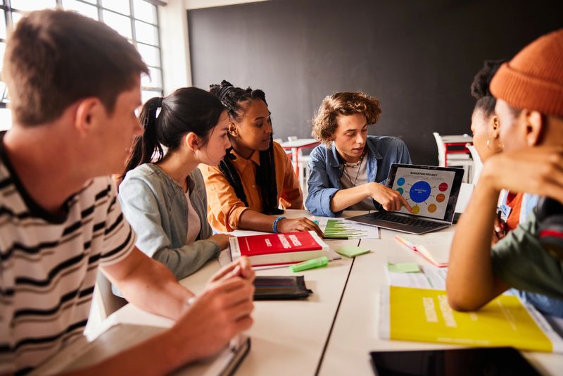 Diverse group of students working on a marketing project together on a laptop during a break between classes at school
