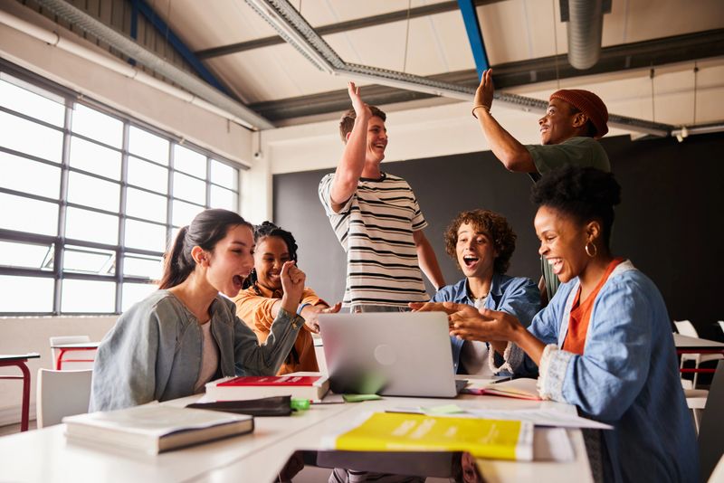 Diverse group of students cheering and high-fiving each other during a break from studying in a school classroom