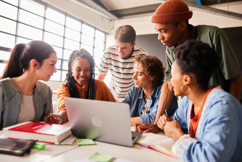 Diverse group of smiling students working together on a laptop during a study break between classes at school