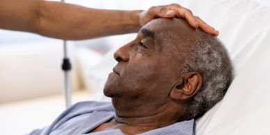 Elderly man lying in bed with hand on forehead.