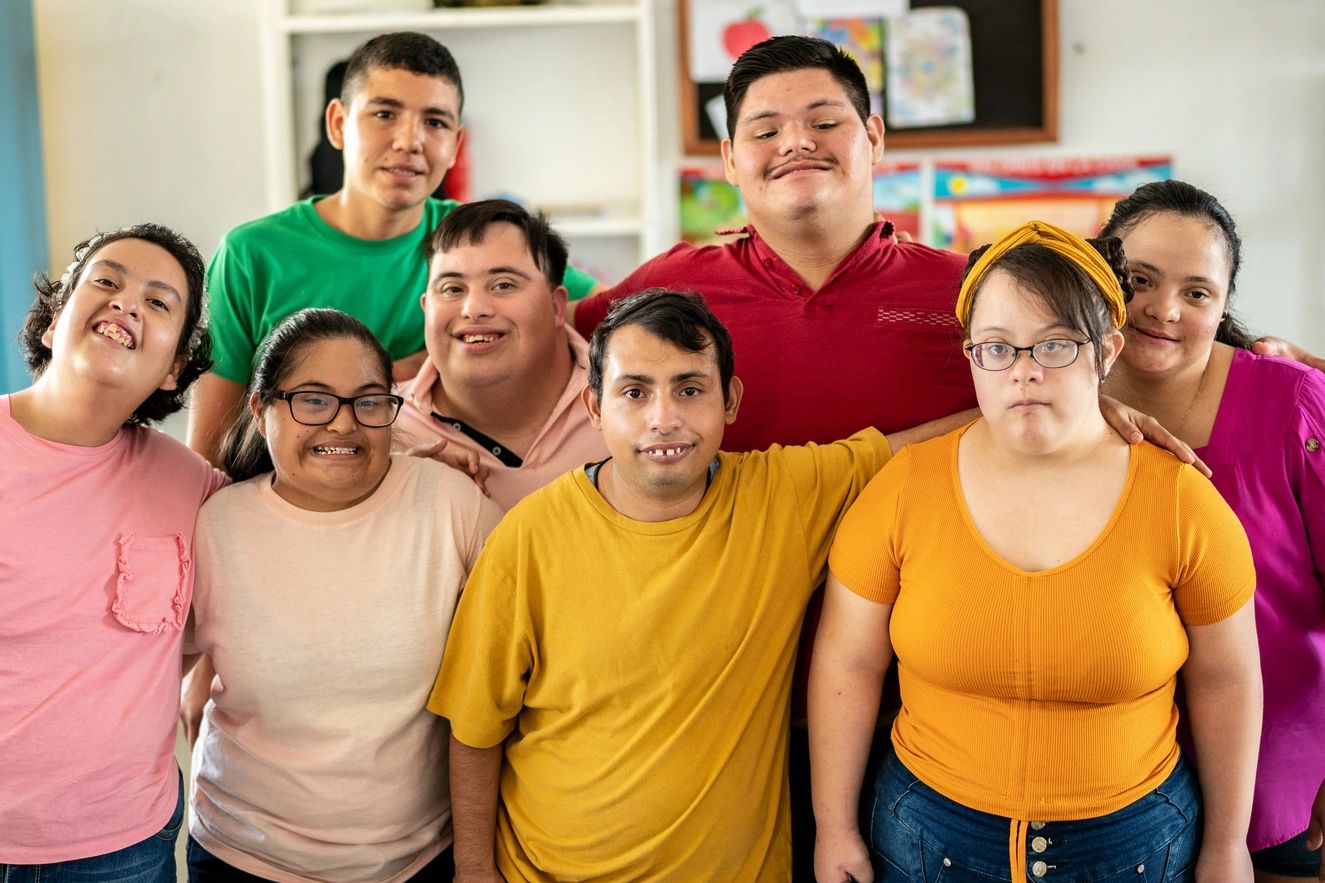 A diverse group of smiling young adults posing together in a classroom.