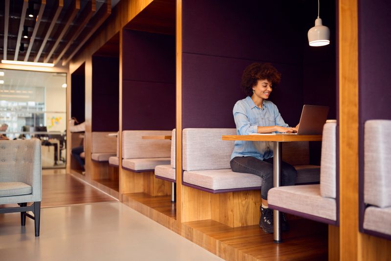 Young Businesswoman In Modern Open Plan Office Working On Laptop In Seating Pod