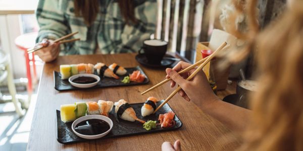 Two people eating sushi with chopsticks at a wooden table.